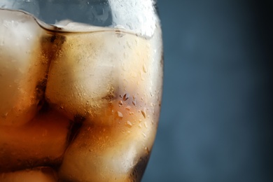 Photo of Refreshing cola with ice in glass on color background, closeup. Space for text