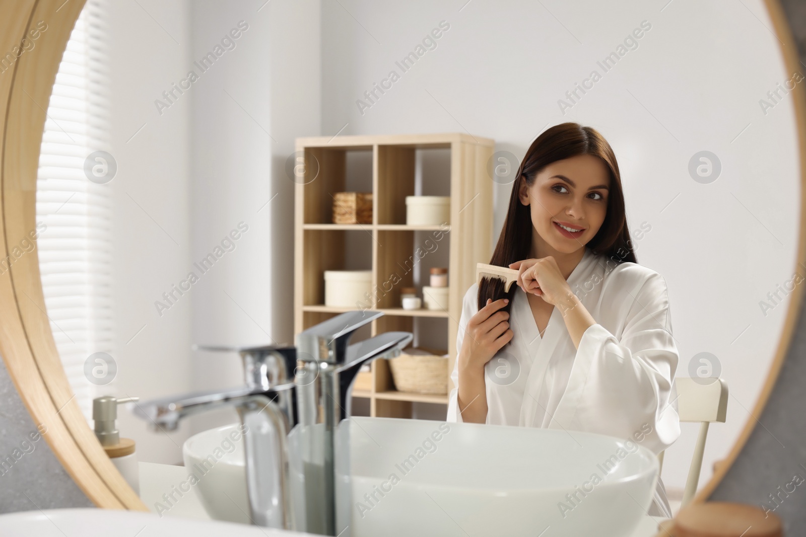 Photo of Beautiful woman brushing her hair near mirror in bathroom, space for text