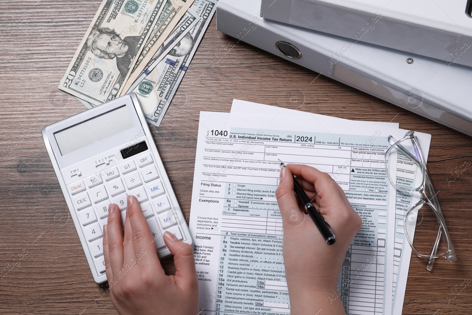 Photo of Payroll. Woman using calculator while working with tax return forms at wooden table, top view