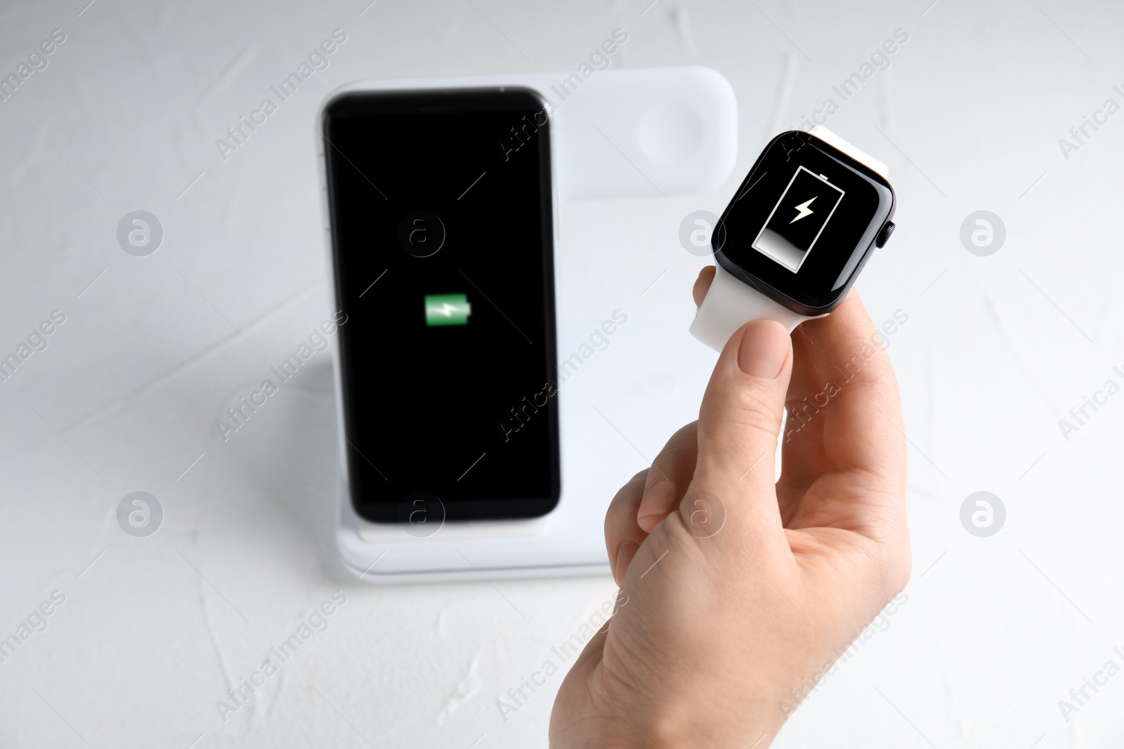 Photo of Woman taking smartwatch from wireless charger at white stone table, closeup