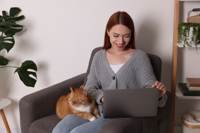 Happy woman with cat working in armchair at home