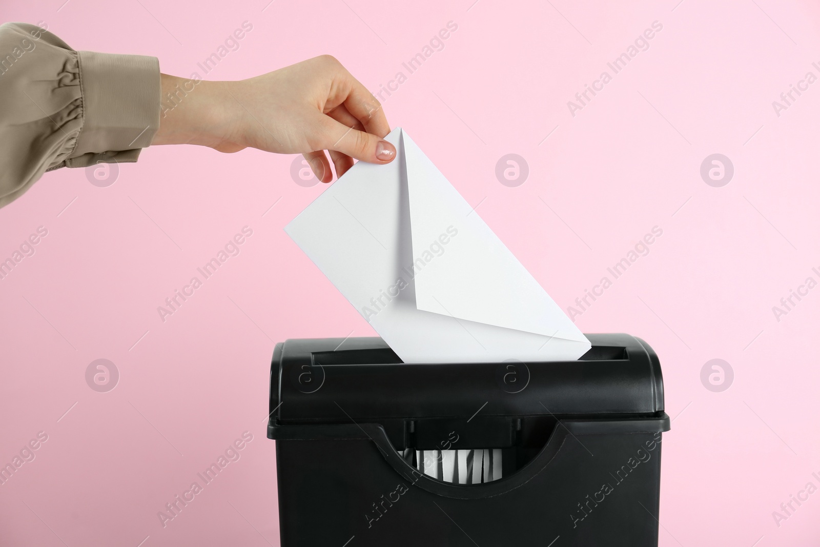 Photo of Woman destroying envelope with shredder on pink background, closeup