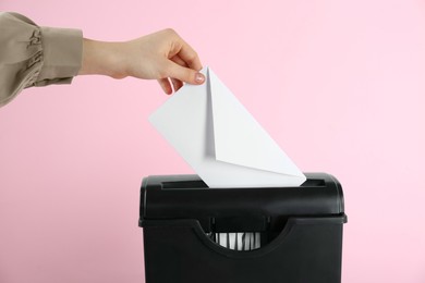 Photo of Woman destroying envelope with shredder on pink background, closeup