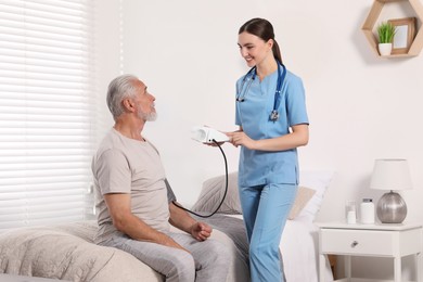 Young healthcare worker measuring senior man's blood pressure indoors