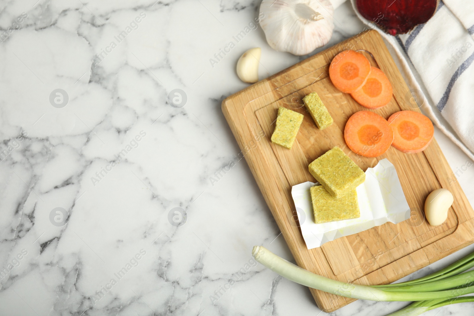 Photo of Bouillon cubes and other ingredients on white marble table, flat lay. Space for text