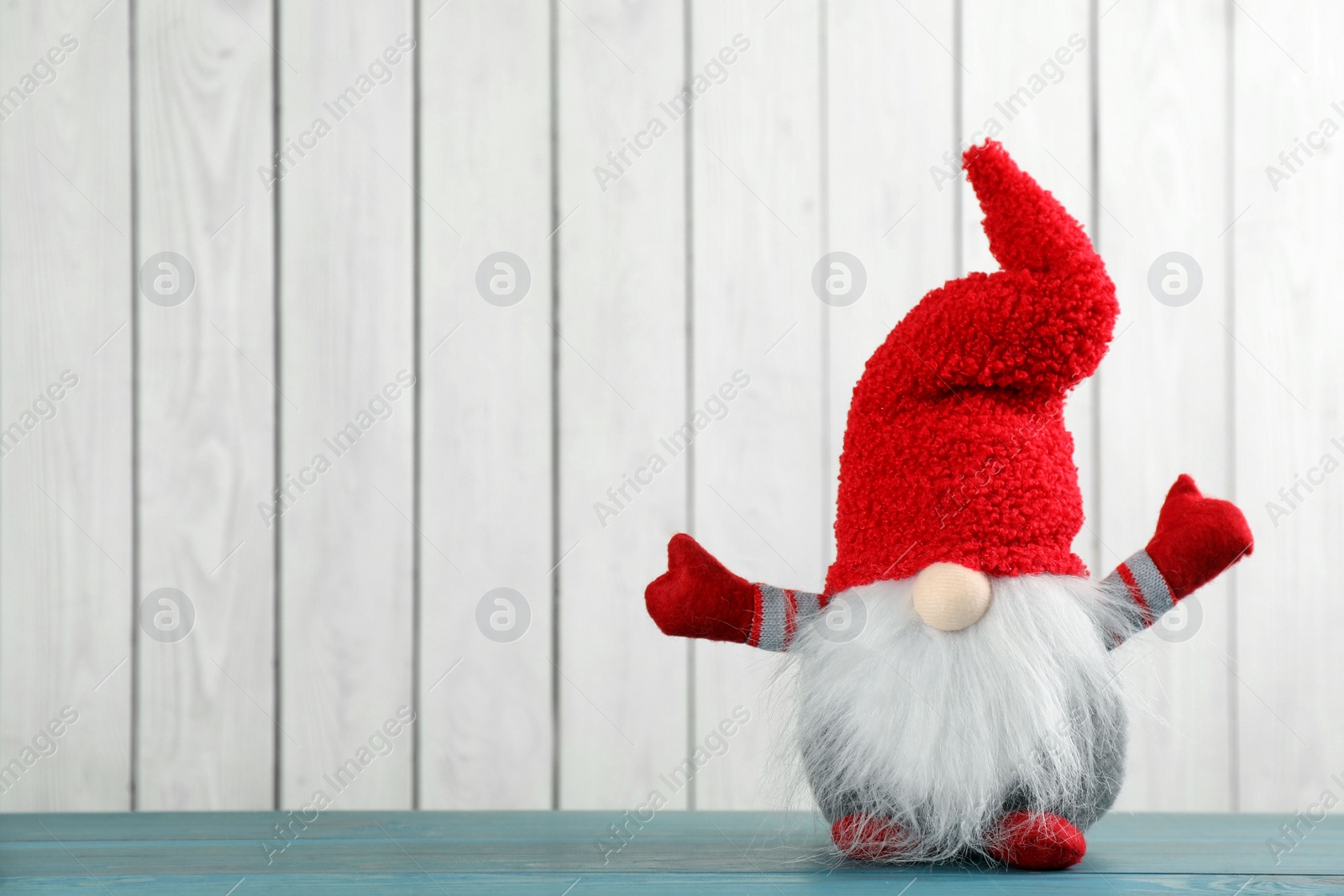 Photo of Cute Christmas gnome on turquoise table against white wooden background. Space for text