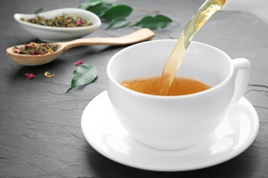 Photo of Pouring aromatic tea into cup on black table, closeup