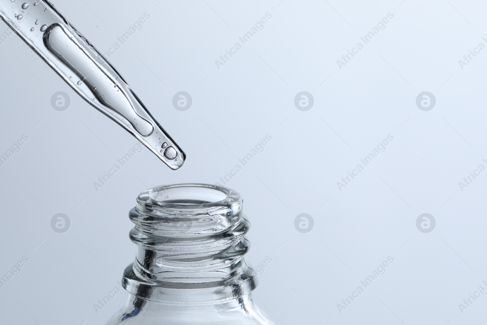 Photo of Dripping liquid from pipette into glass bottle on light blue background, closeup. Space for text