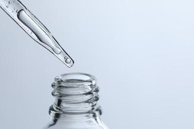 Photo of Dripping liquid from pipette into glass bottle on light blue background, closeup. Space for text