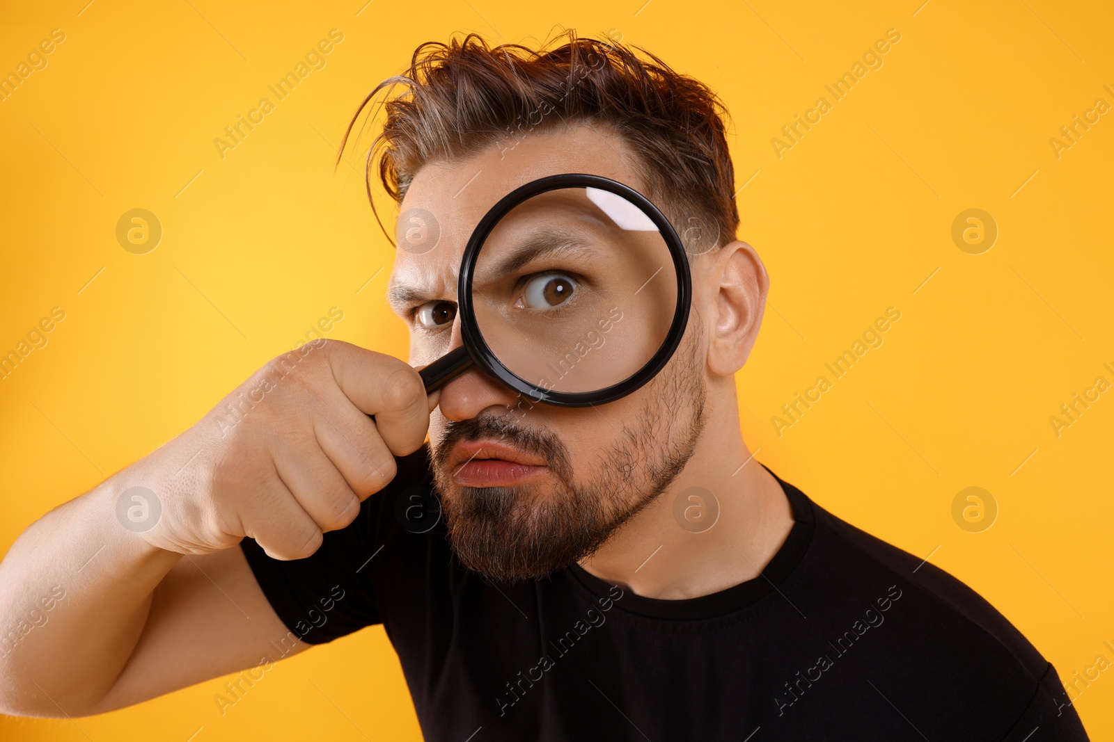 Photo of Handsome man looking through magnifier on yellow background