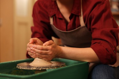 Woman crafting with clay on potter's wheel indoors, closeup