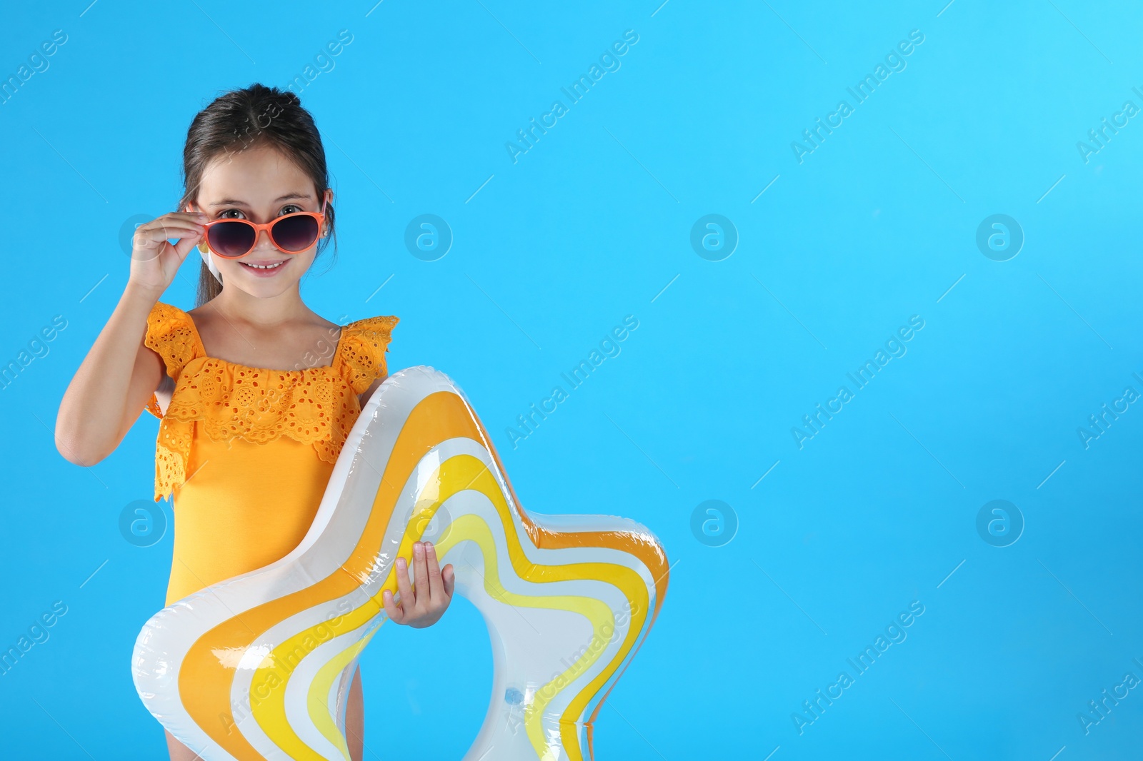 Photo of Cute little child in beachwear with inflatable ring on light blue background. Space for text