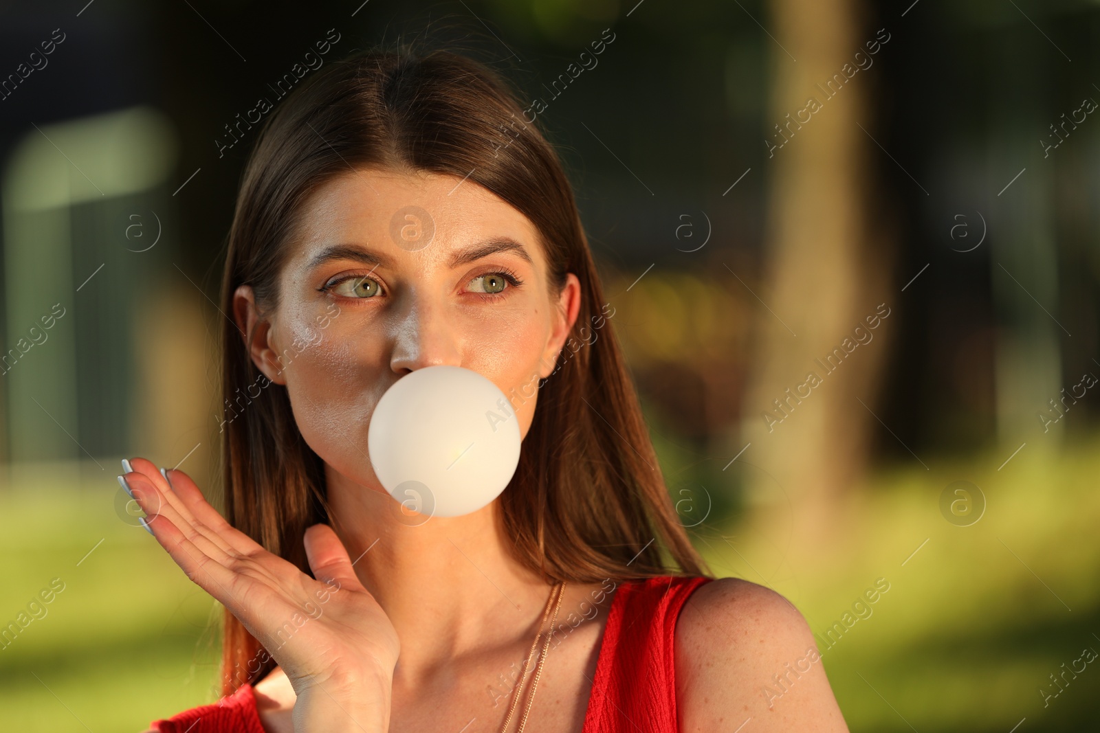 Photo of Beautiful young woman blowing bubble gum in park. Space for text