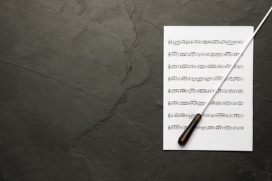 Conductor's baton and sheet music on black background, top view. Space for text