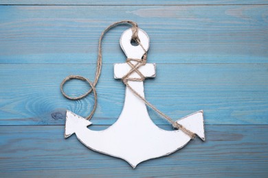 Photo of White anchor with hemp rope on light blue wooden table, top view