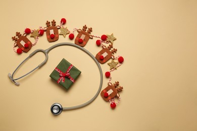 Photo of Greeting card for doctor with stethoscope, gift box and Christmas decor on beige background, flat lay. Space for text