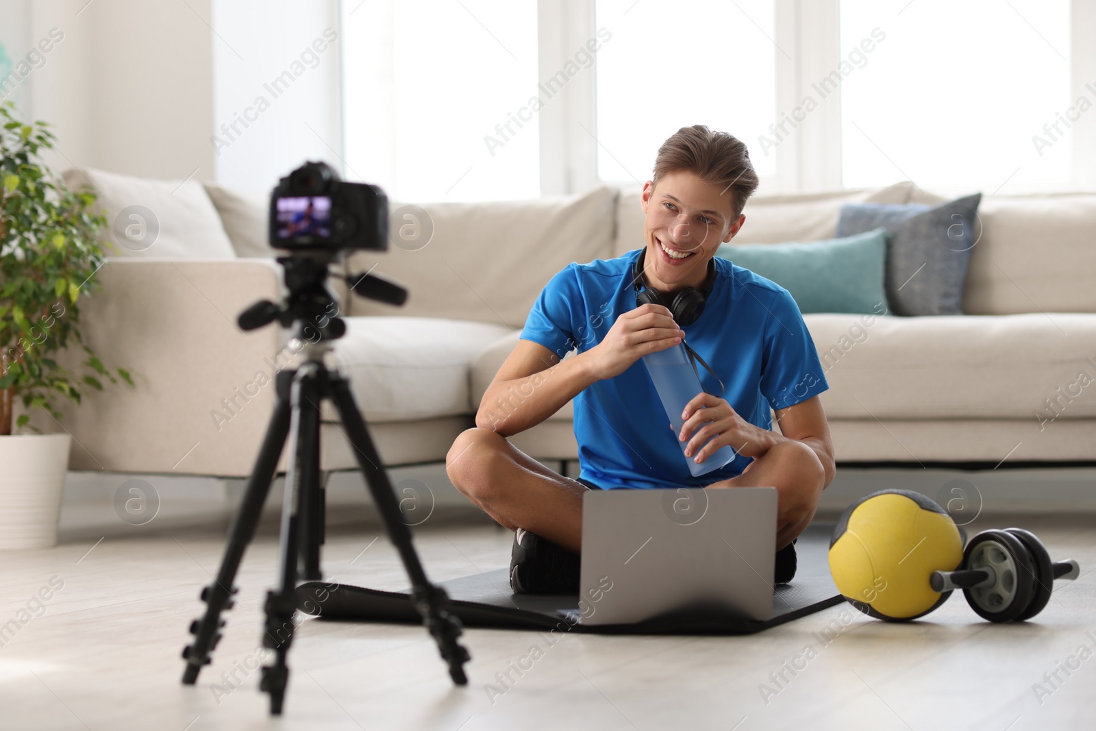 Photo of Smiling sports blogger recording fitness lesson with camera at home