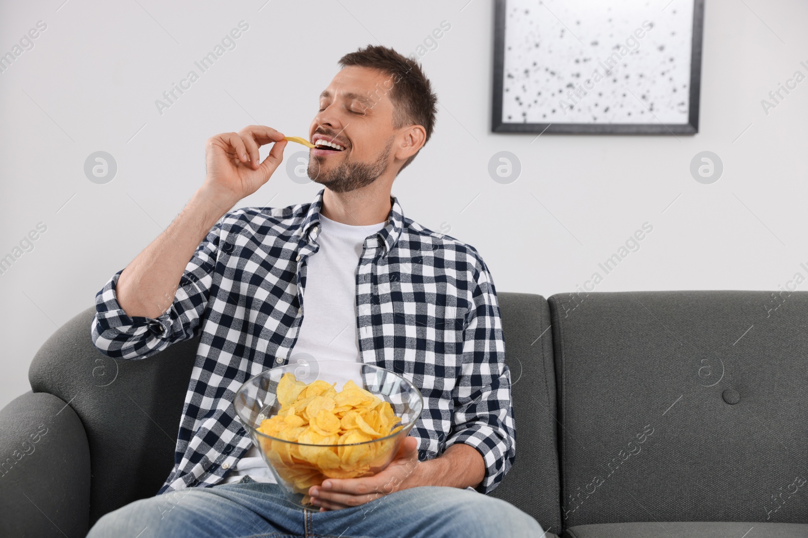 Photo of Handsome man eating potato chips on sofa at home