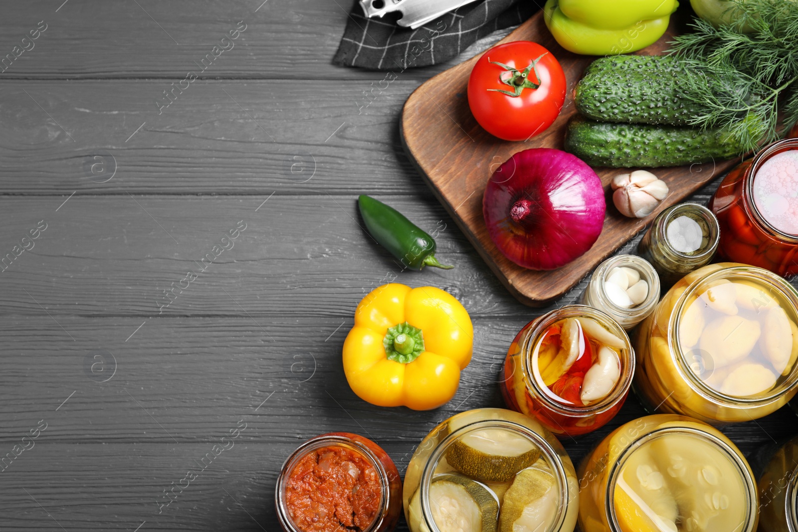 Photo of Flat lay composition with jars of pickled vegetables on grey wooden table. Space for text