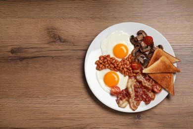 Photo of Plate of fried eggs, mushrooms, beans, tomatoes, bacon and toasts on wooden table, top view with space for text. Traditional English breakfast