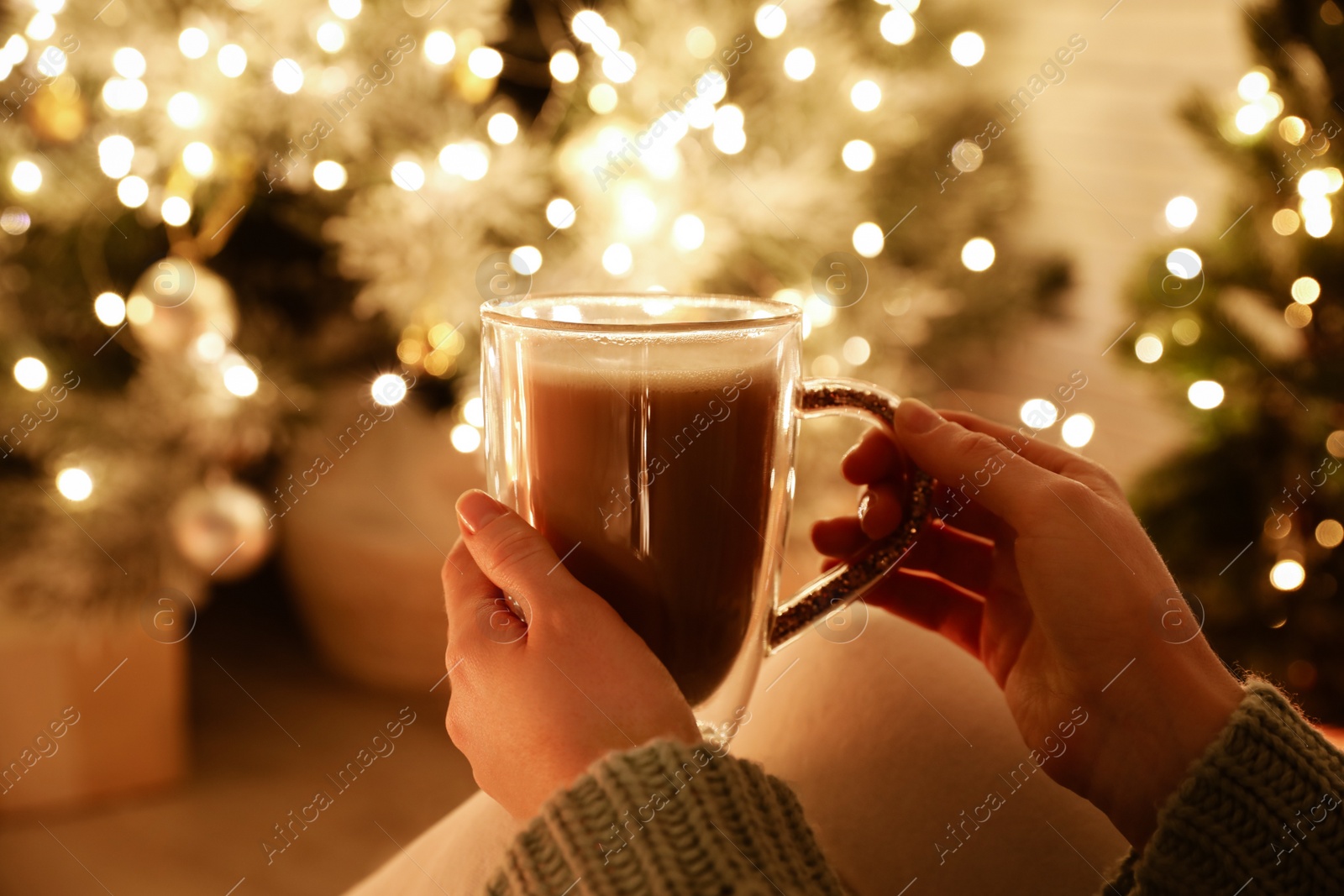 Photo of Woman with cup of drink and blurred Christmas lights on background, closeup