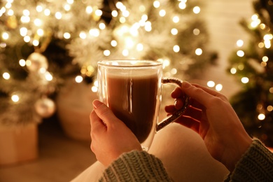 Woman with cup of drink and blurred Christmas lights on background, closeup