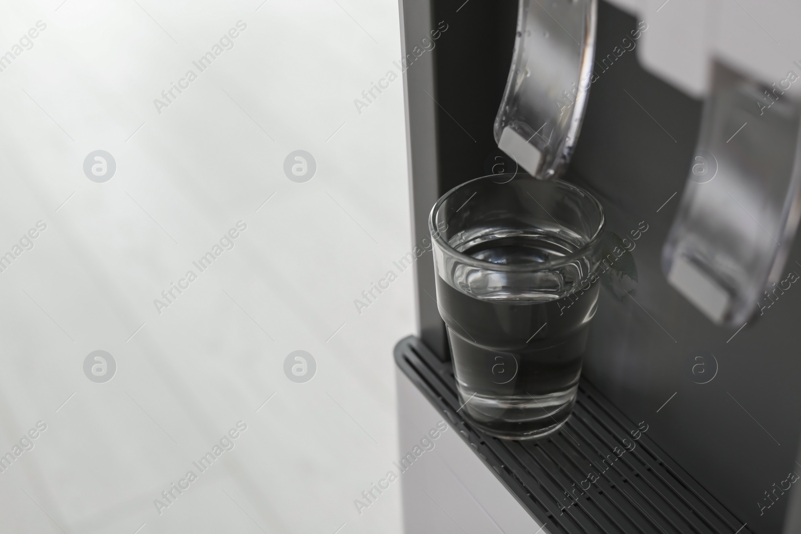 Photo of Modern water cooler with glass indoors, closeup. Space for text