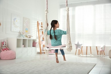 Photo of Cute little girl playing on swing at home