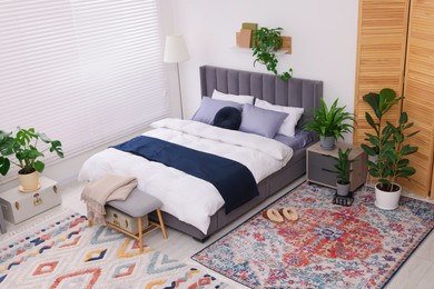 Stylish bedroom with double bed and beautiful green houseplants, above view. Modern interior