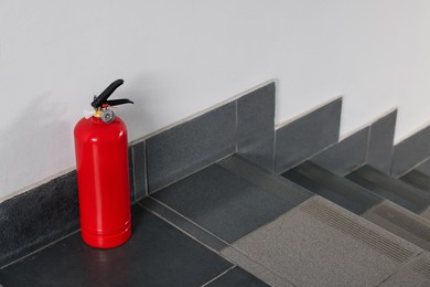 Red fire extinguisher near white wall, space for text