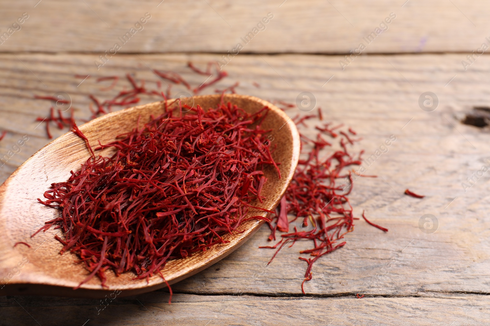 Photo of Aromatic saffron and spoon on wooden table, closeup