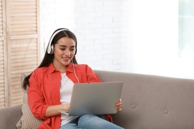 Photo of Young woman with headphones and laptop on sofa in living room