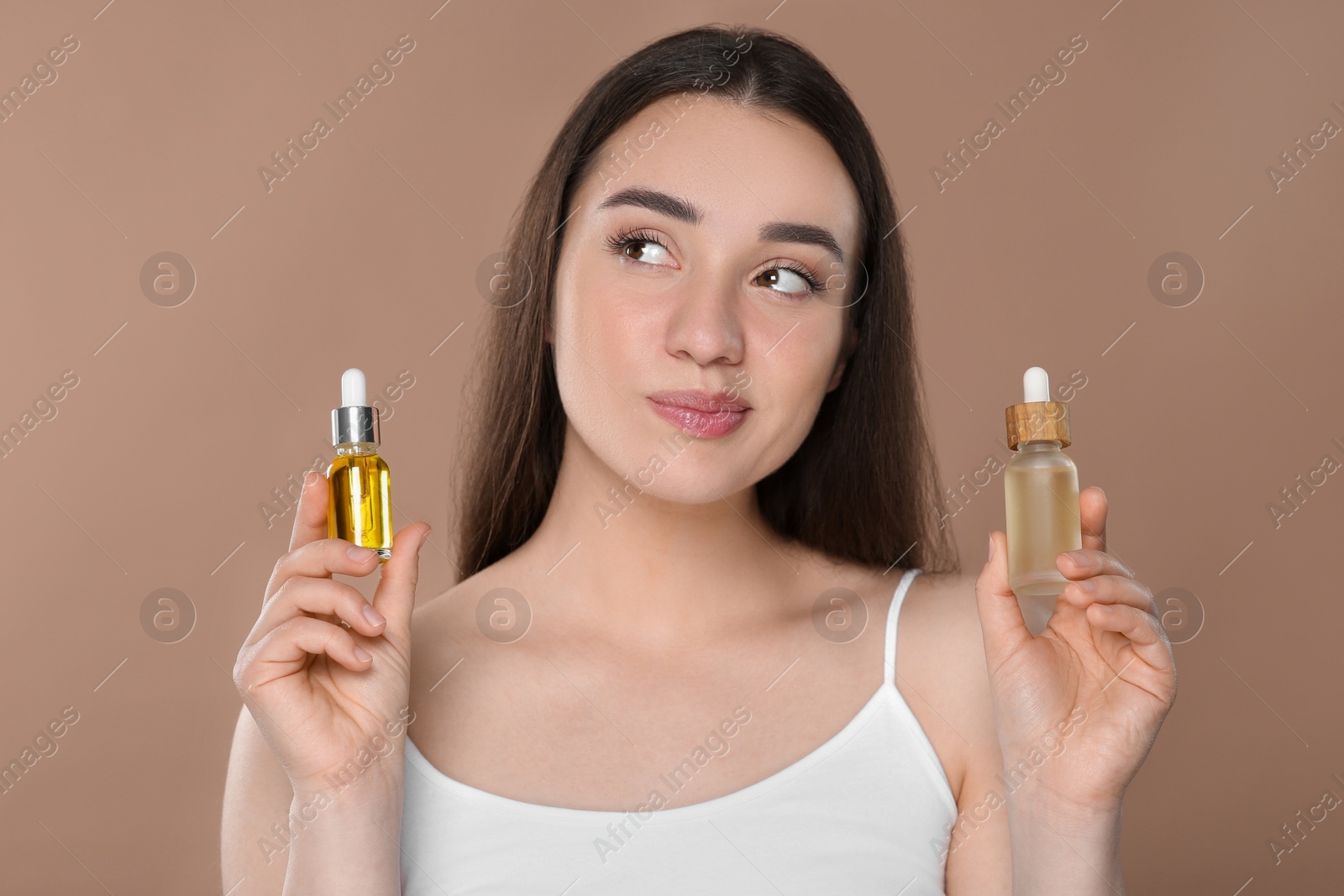 Photo of Woman with bottles of essential oil on brown background