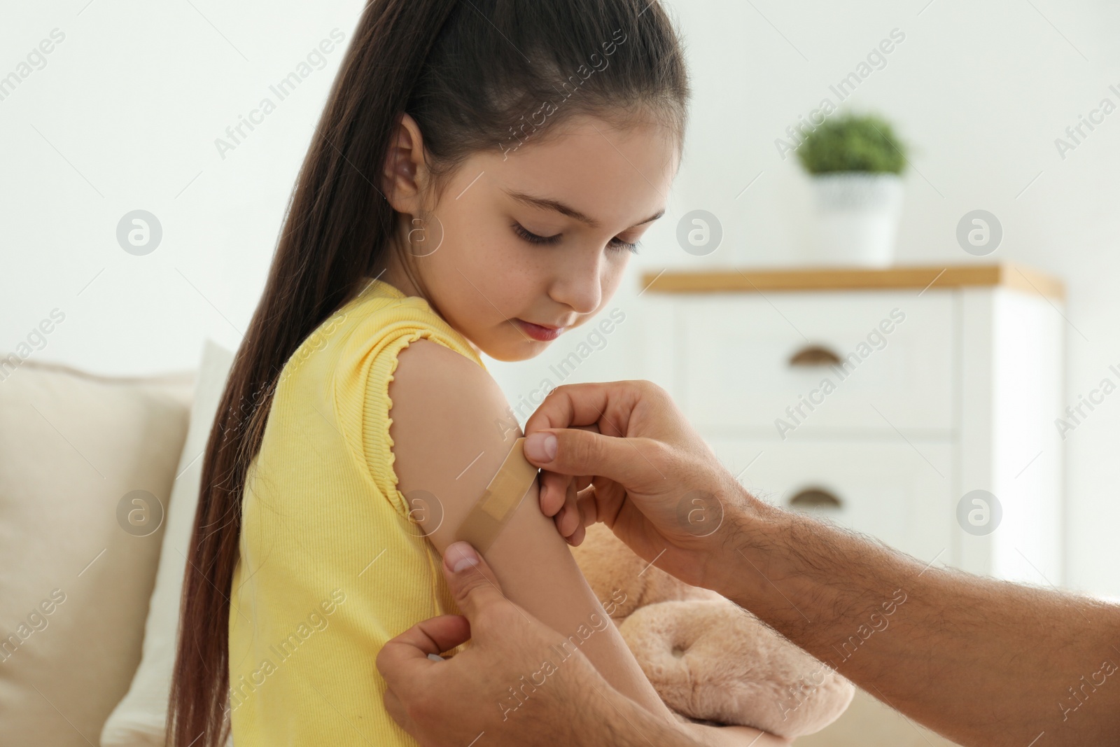 Photo of Father putting sticking plaster onto daughter's arm at home