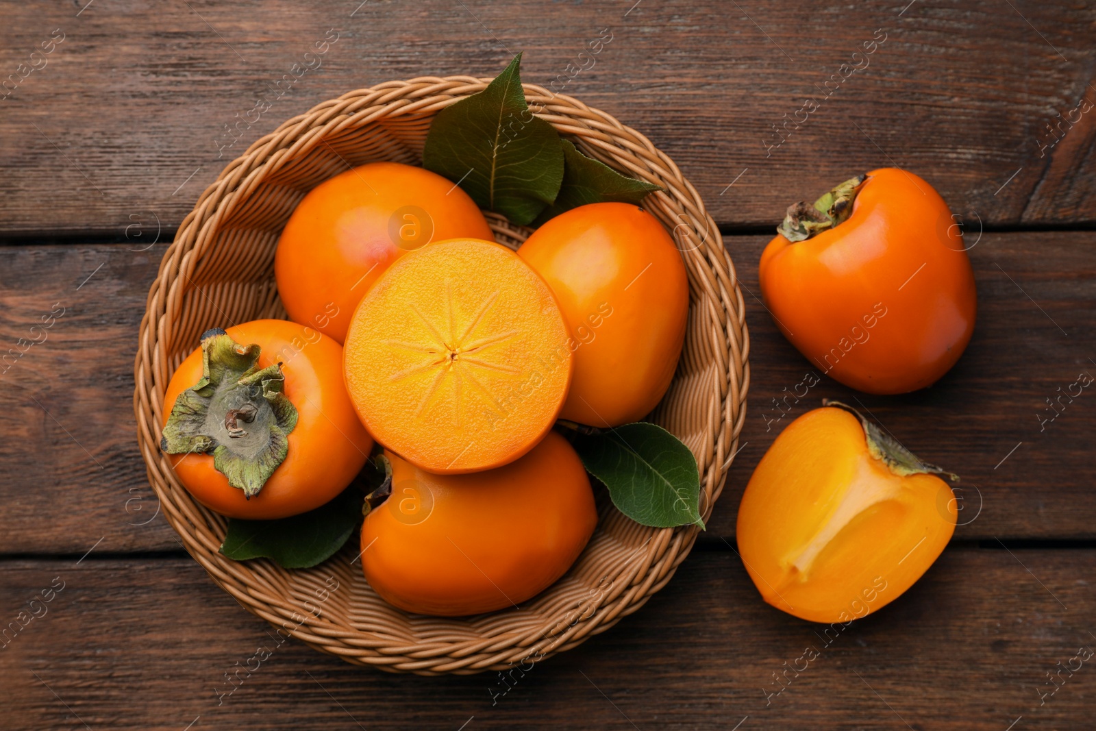 Photo of Delicious ripe persimmons in wicker basket on wooden table, flat lay
