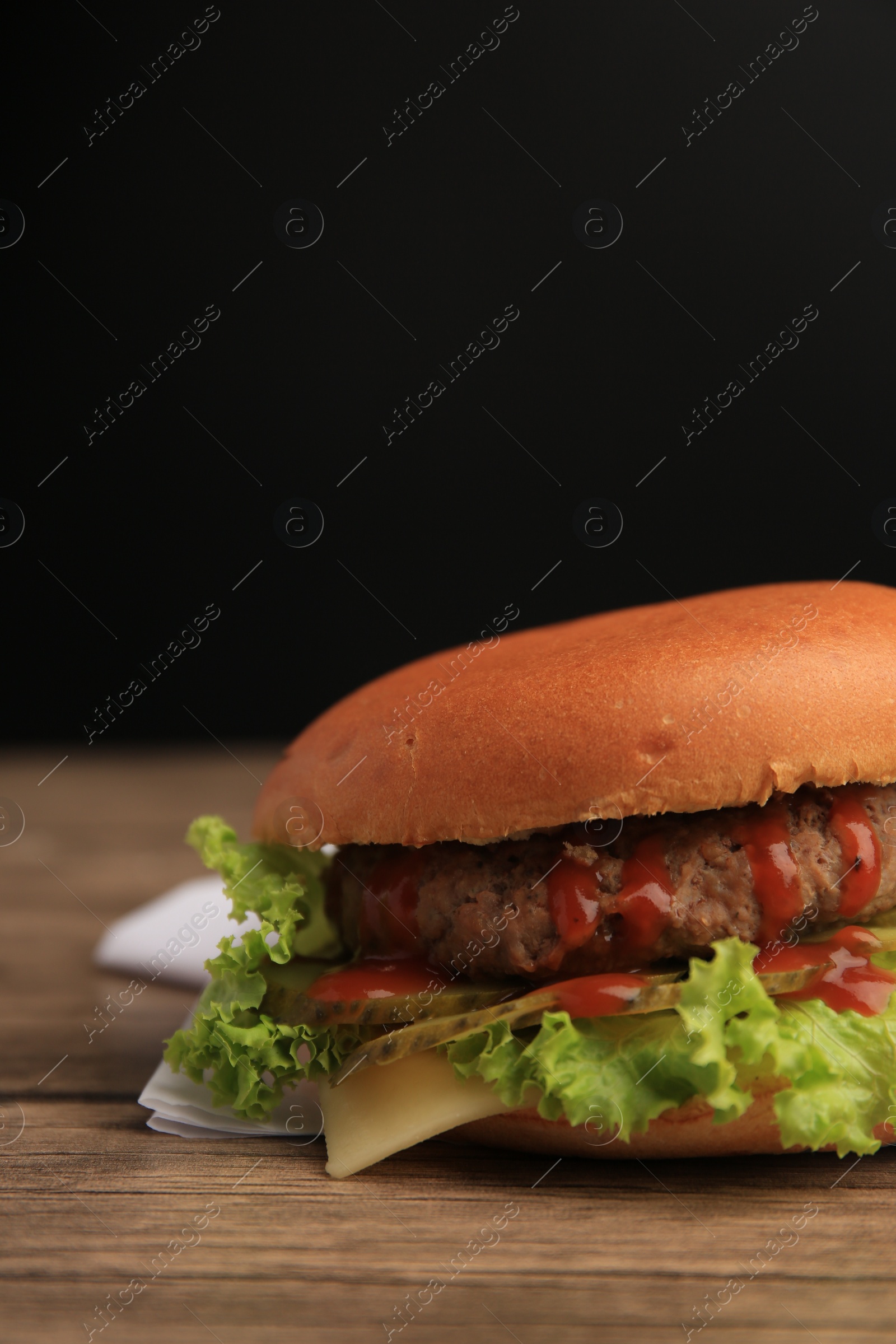 Photo of One tasty burger with patty, lettuce and cheese on wooden table, closeup. Space for text