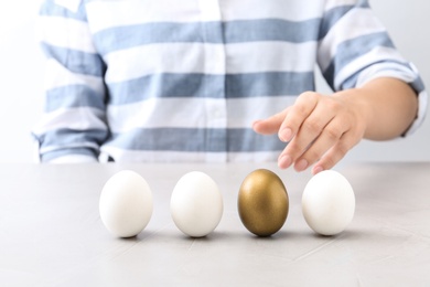 Woman choosing golden egg from white ones at table, closeup