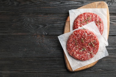 Photo of Raw meat cutlets for burger on black wooden table, top view. Space for text