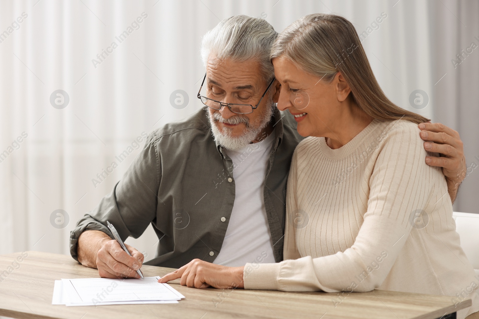 Photo of Senior couple signing Last Will and Testament indoors