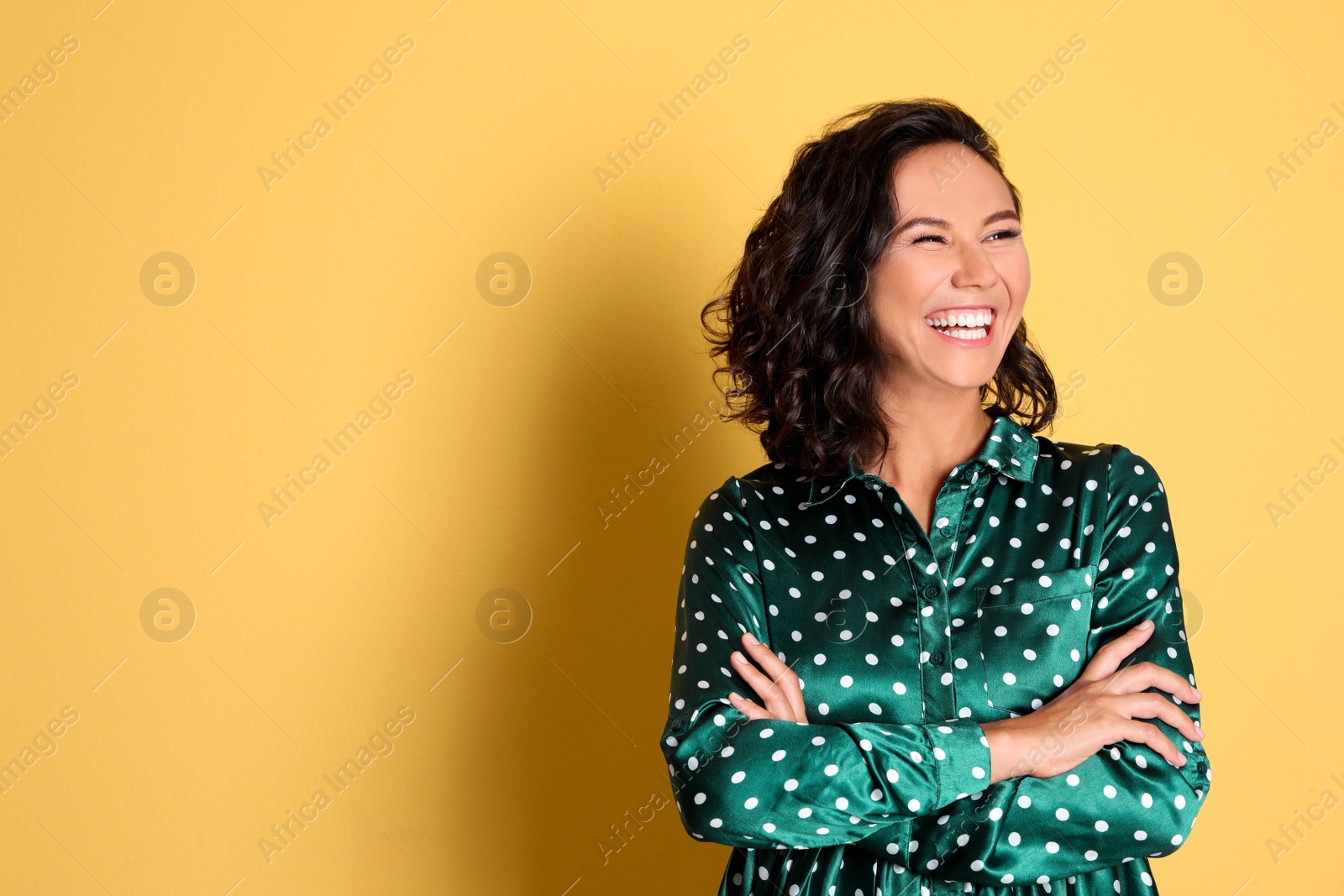 Photo of Happy young woman with crossed hands on yellow background. Space for text