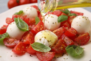 Photo of Pouring oil onto tasty salad Caprese with tomatoes, mozzarella balls and basil, closeup