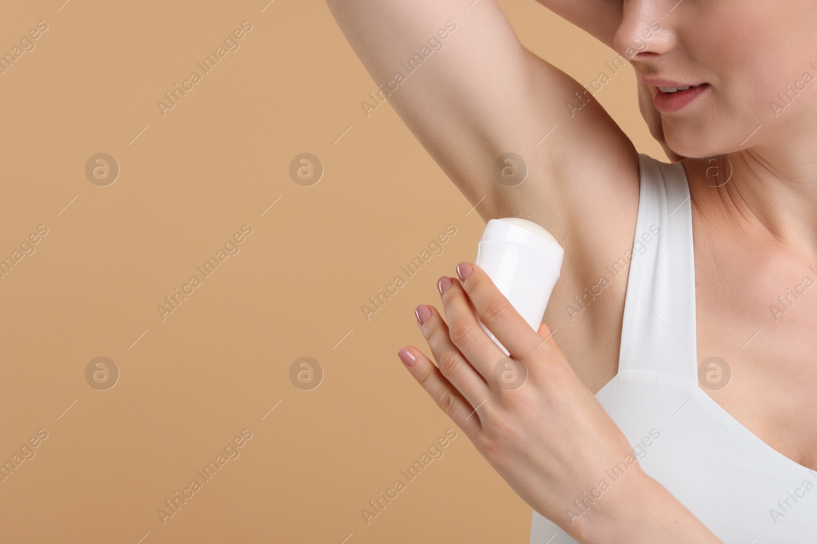 Photo of Woman applying deodorant on beige background, closeup. Space for text