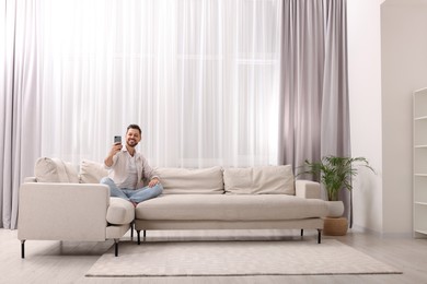 Photo of Man taking selfie near window with beautiful curtains in living room