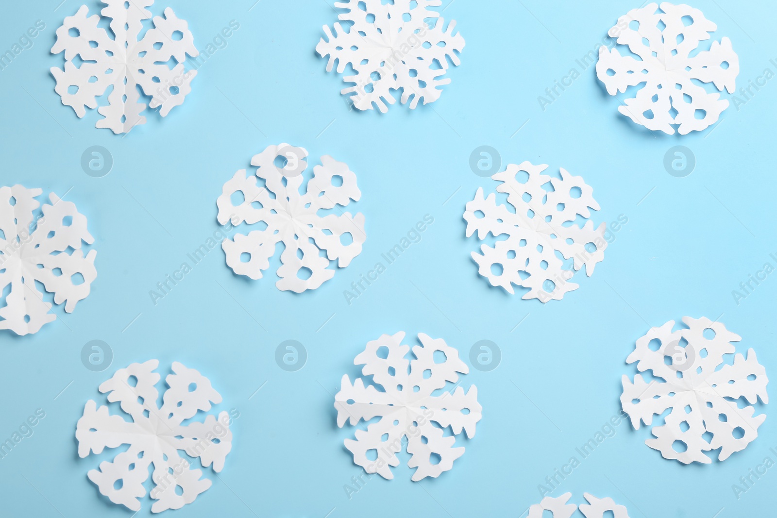 Photo of Many paper snowflakes on light blue background, flat lay