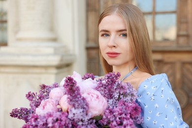 Photo of Beautiful woman with bouquet of spring flowers near building outdoors, space for text