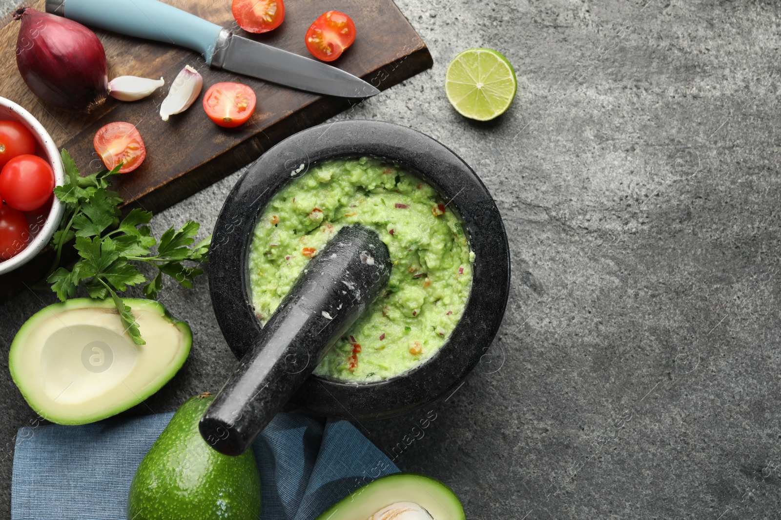 Photo of Mortar with delicious guacamole and ingredients on grey table, flat lay. Space for text