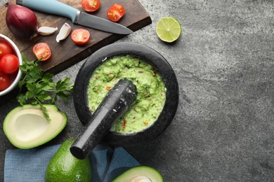 Photo of Mortar with delicious guacamole and ingredients on grey table, flat lay. Space for text