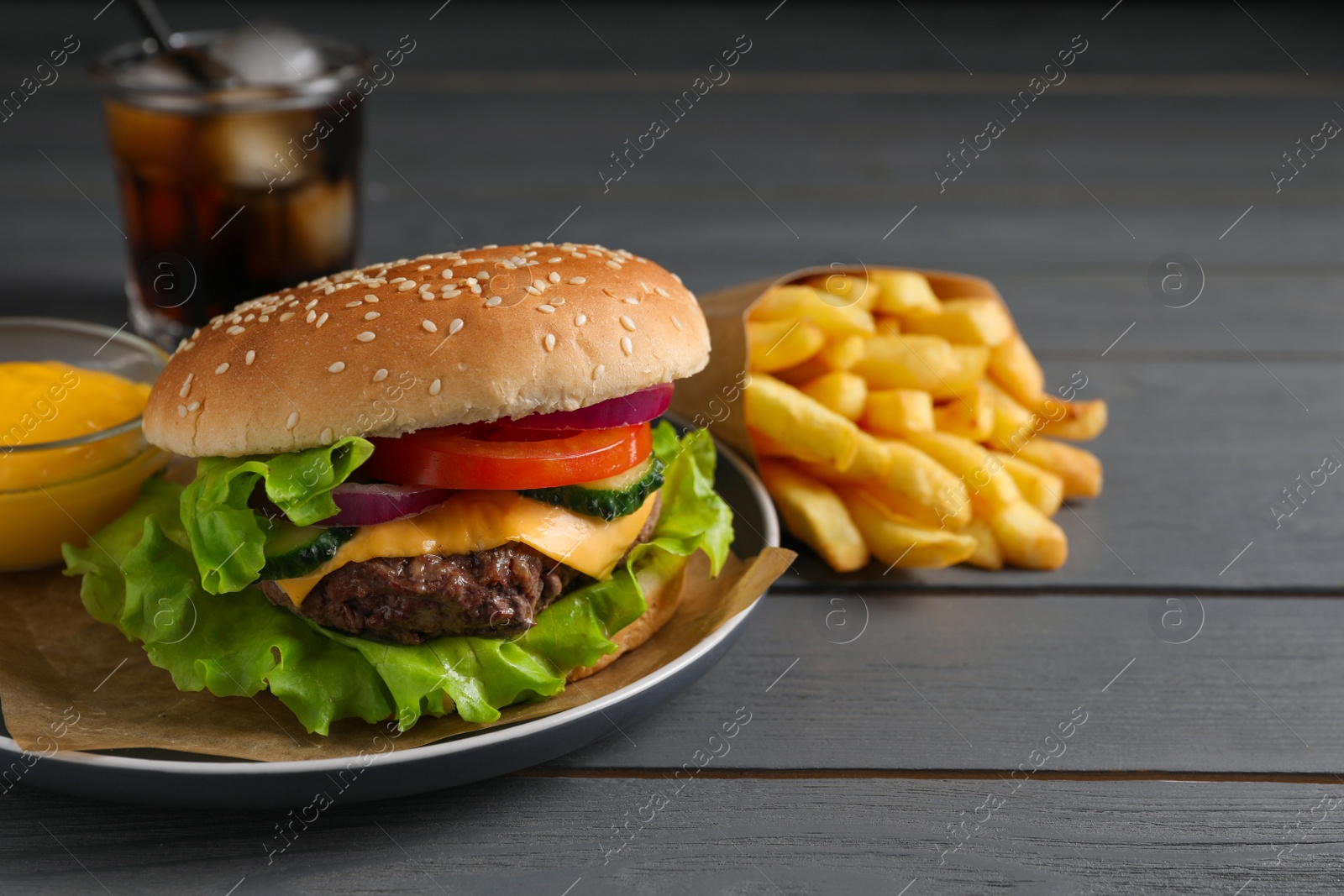 Photo of Delicious burger, soda drink and french fries served on grey wooden table. Space for text