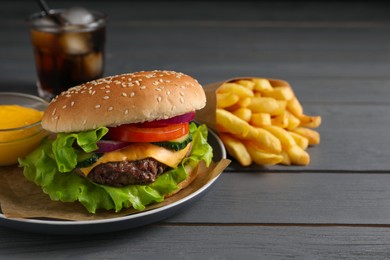 Delicious burger, soda drink and french fries served on grey wooden table. Space for text