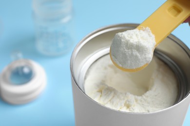 Photo of Scoop of powdered infant formula over can on light blue background, closeup. Baby milk